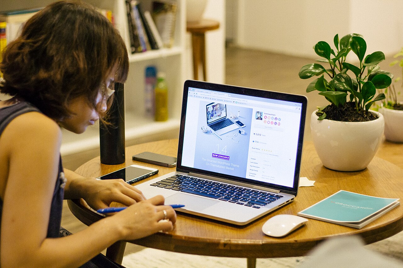 A person taking notes beside a laptop at a coffee table